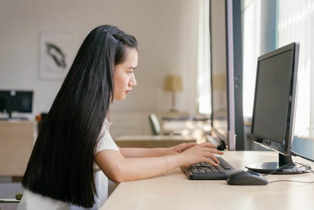 A focused student typing on a desktop computer, researching German articles definite VS indefinite for grammar clarity.