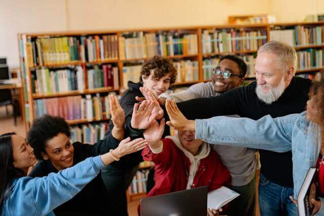 A group of students celebrating their understanding of the German verb 'haben' after a successful study session in a library.