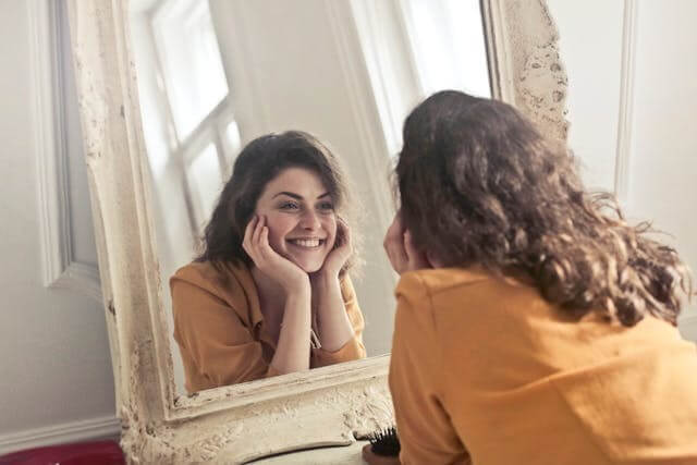 A smiling woman looking in the mirror symbolising happiness for the German Emotions Vocabulary Quiz.