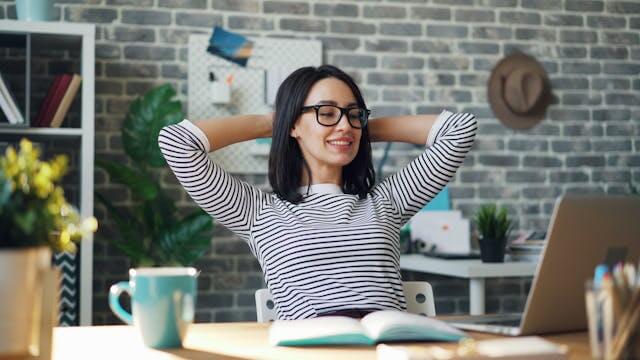 A smiling woman taking a break after studying the German accusative case with online grammar exercises on her laptop.