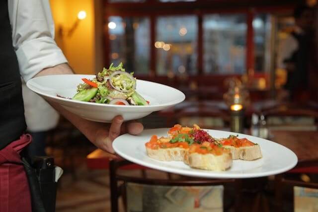 A waiter serving dishes of salad and bruschetta in a restaurant, symbolising A German Short Story featuring Restaurant Vocabulary.