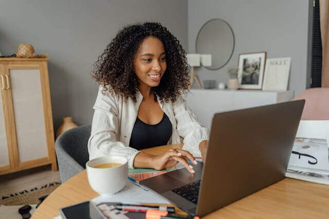 A woman practicing German genitive verbs on a laptop at her desk with study materials and coffee.