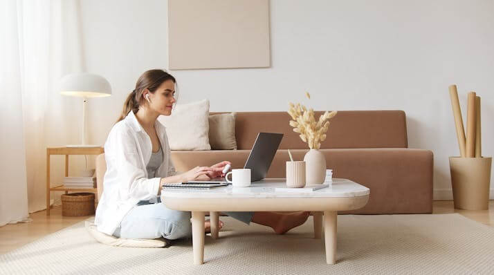 A woman sitting on the floor using a laptop, symbolizing focused learning for the Important German Verbs Vocabulary Quiz.