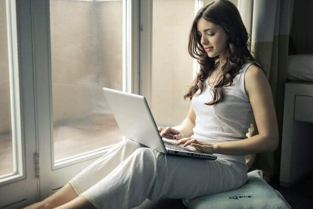 A woman studying the German genitive case while sitting by a window and using a laptop for grammar exercises.