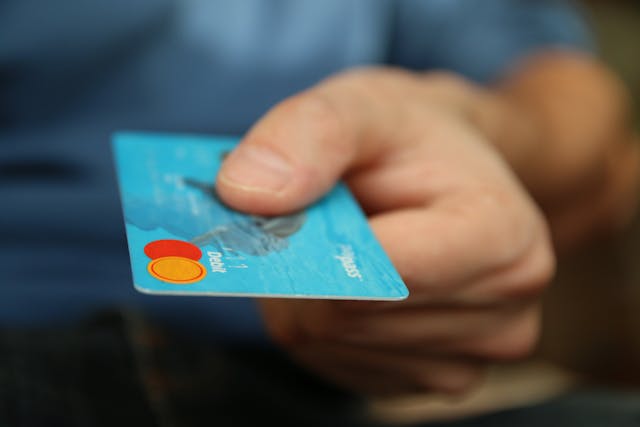 Close-up of a hand holding a blue credit card, representing payment methods in German vocabulary for shopping.