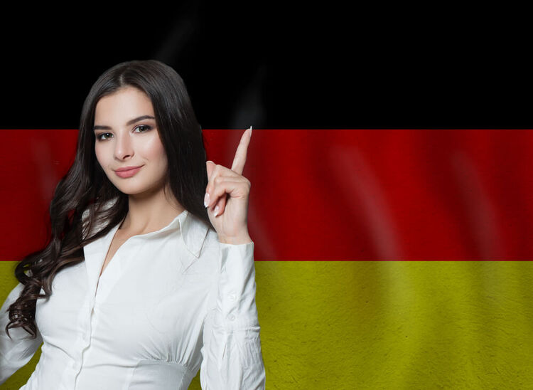 Confident woman pointing upwards in front of a German flag, symbolizing mastery of German relative clauses.