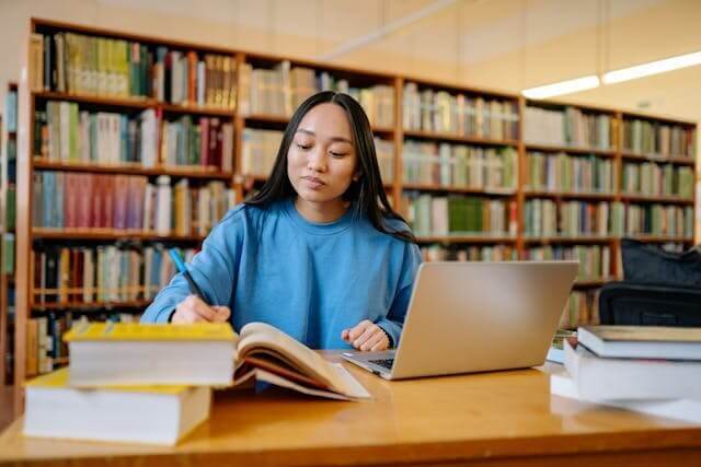 Focused student studying with books and a laptop to show engagement with our German prepositions quiz.