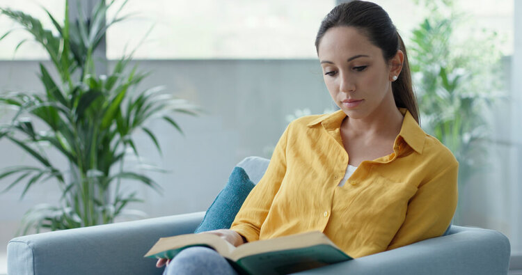 Focused woman sitting on a couch reading a book, representing the study of German articles der, die, and das.