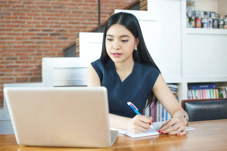 Focused woman writing notes while studying a German articles quiz on her laptop.