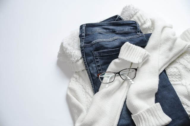 Folded jeans, sweater, and glasses on a white background, symbolising the German Short Story featuring Clothing Vocabulary.