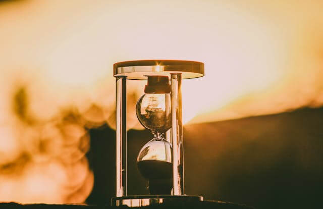 Hourglass against a sunset, illustrating German temporal prepositions like 'seit' (since) and 'bis' (until).