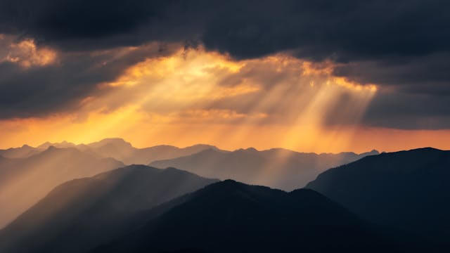 Mountain landscape with sun rays shining through clouds, symbolizing contrast in German concessive clauses.