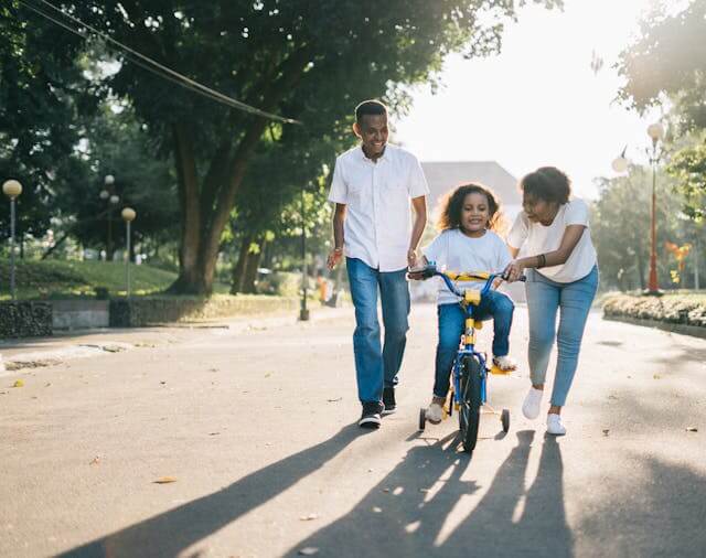 Parents teaching their child to ride a bike in the park - German Family Vocabulary.