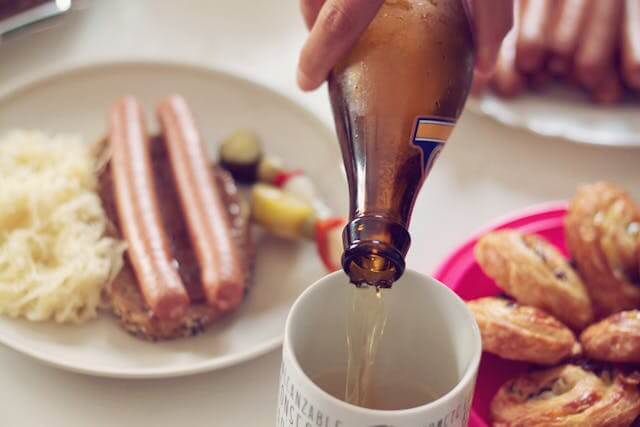 Traditional German meal with sausages, sauerkraut, and a hand pouring beer into a mug, illustrating German Food Vocabulary.