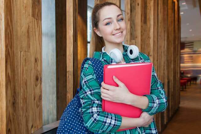 Smiling female student holding a red folder, symbolizing German vocabulary for education and learning.