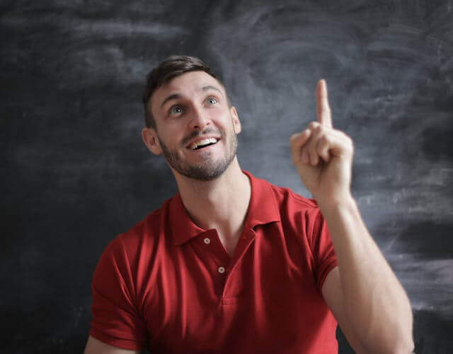 Smiling man pointing upwards in front of a chalkboard, symbolizing explanation of German Final Clauses.