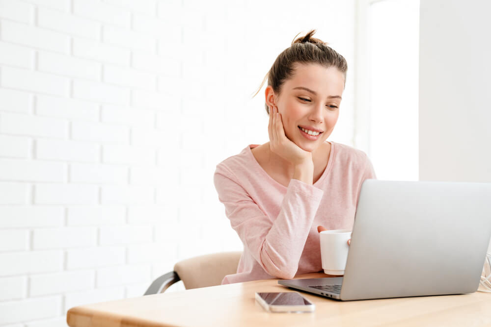 Smiling woman learning German N-Declension rules on her laptop at home.