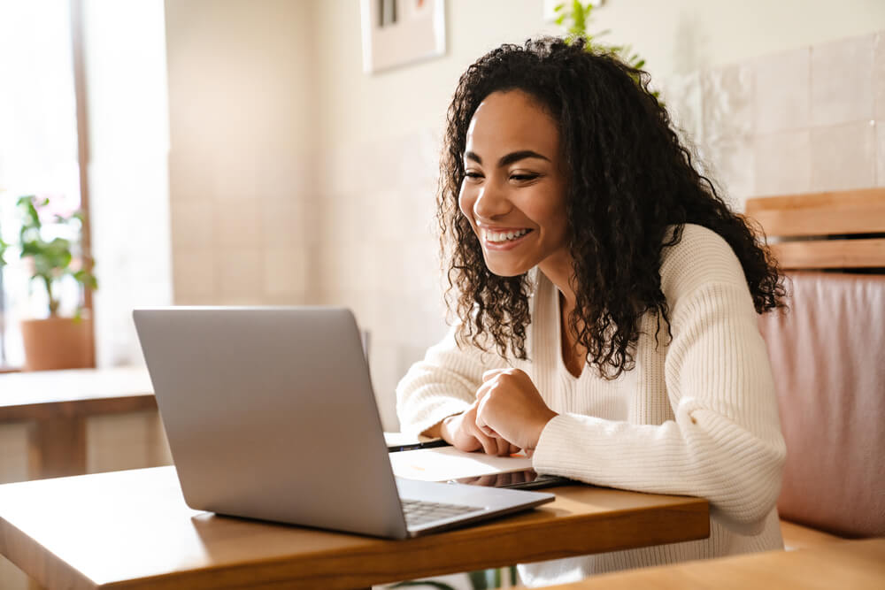 Smiling woman learning the German Future 1 Tense while working on her laptop in a cozy café.