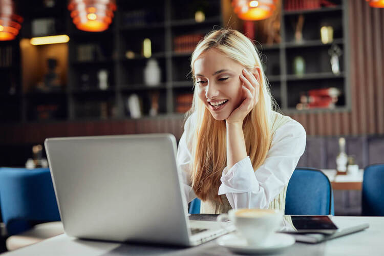 Smiling woman sitting at a table using a laptop to study a German articles quiz for A1-B1 learners.