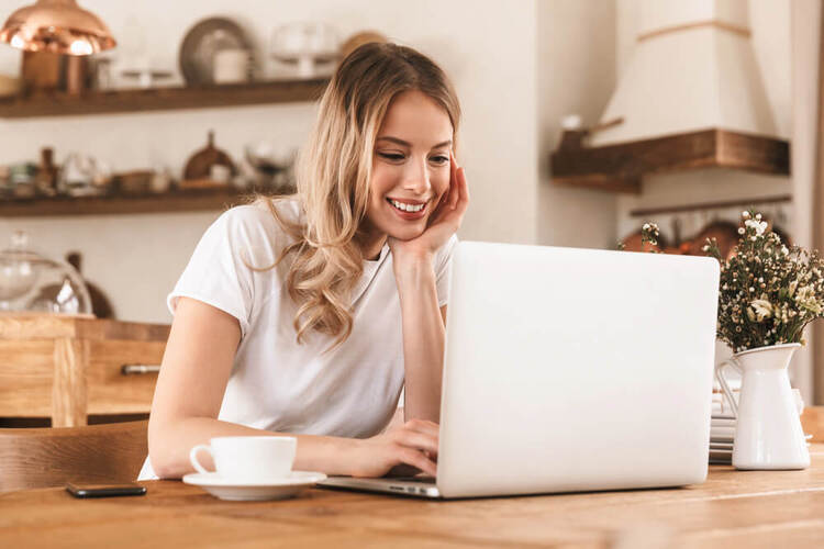 Smiling woman sitting at a wooden desk using a laptop to study advanced rules in a German articles quiz.