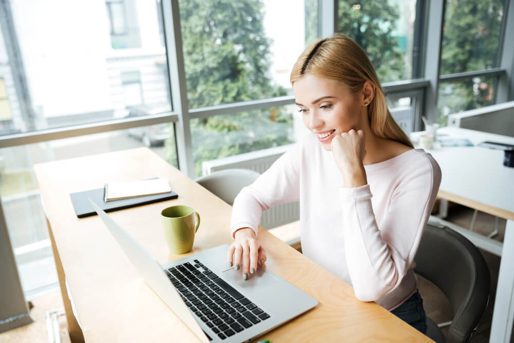 Smiling woman studying the perfect tense in German on a laptop in a modern, bright office setting.