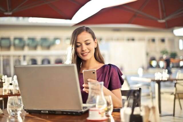 Smiling woman using a laptop and smartphone to show engagement with a German dative and accusative prepositions quiz.