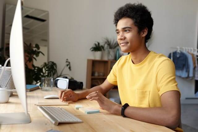 Smiling young man sitting at a desk using a computer to study a German adjective declension quiz