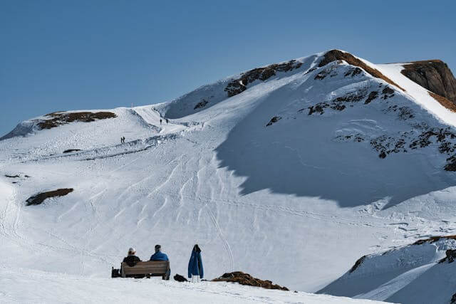 Snow-covered mountain with people enjoying a sunny day, representing German weather vocabulary.