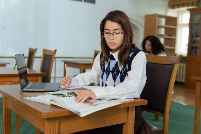 Student studying German inseparable verbs with textbooks and a laptop in a library.