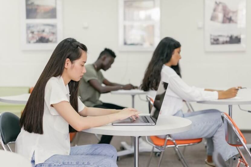 Students practicing German Simple Past Tense on laptops and with written exercises in a classroom setting.