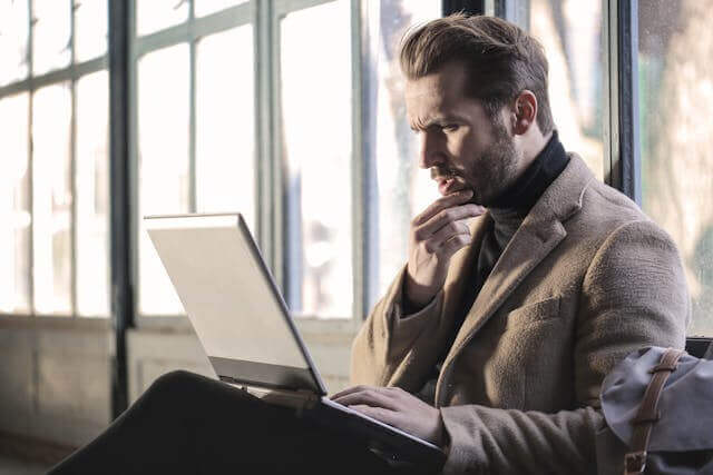 Thoughtful businessman using a laptop to analyze data, illustrating German business vocabulary.