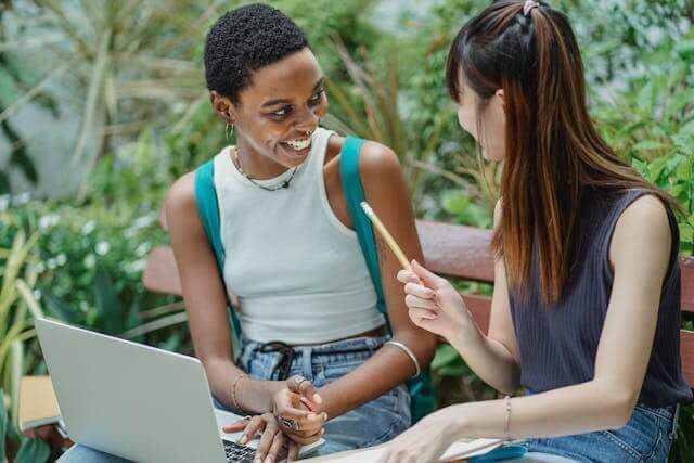 Two students studying German indefinite pronouns together on a laptop in a park setting.