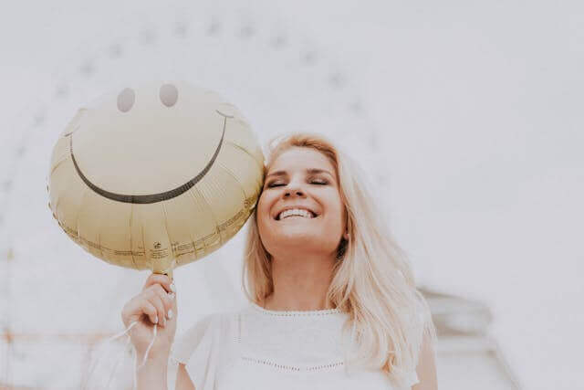 Woman holding a smiley-face balloon, symbolizing happiness and positivity through German adjectives and verbs for emotions and feelings.