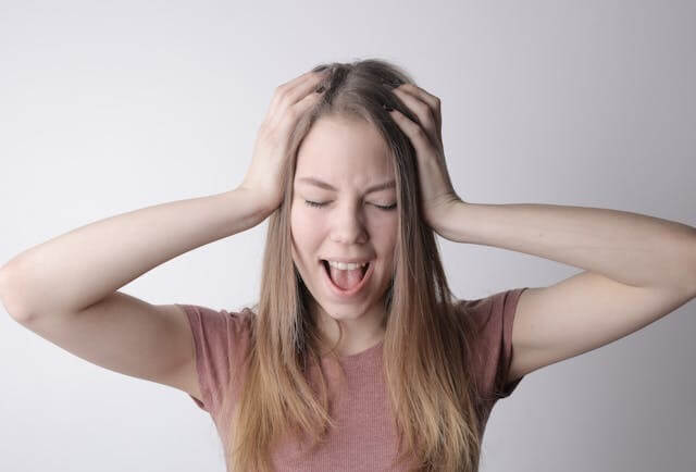 Woman holding her head in frustration to symbolize stress for a German video quiz about stress for B2 learners.