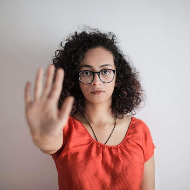 Woman in glasses raising her hand to represent negation with 'Nicht' and 'Kein' in German.