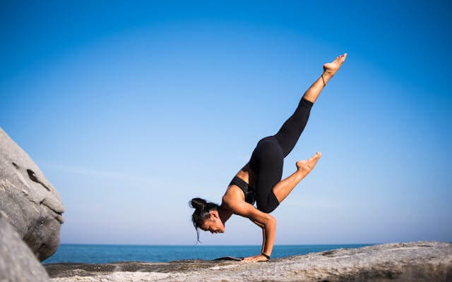 Woman performing yoga on a beach, illustrating German sports vocabulary like Yoga (yoga).