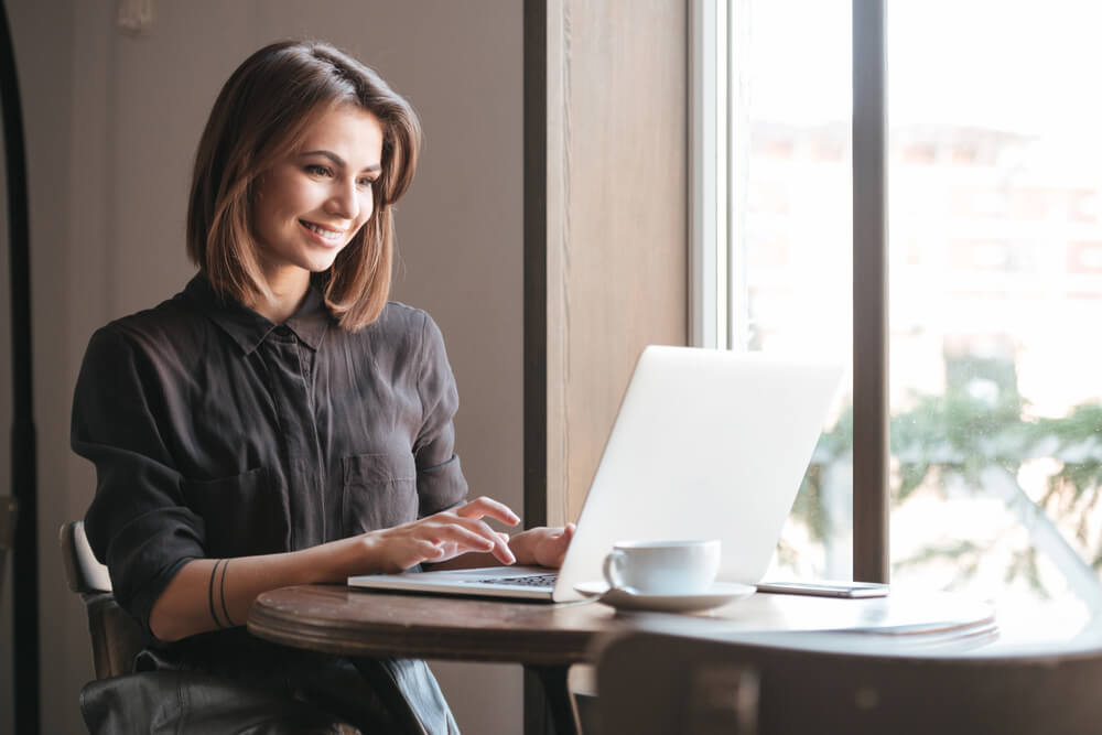 Woman using a laptop in a cafe to practice German relative clauses for advanced grammar skills.