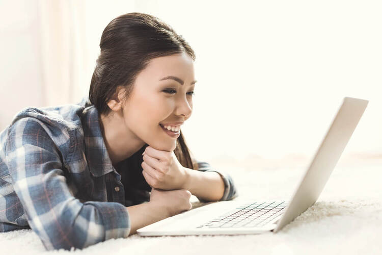 Young woman smiling while studying on a laptop, learning how to form German questions.