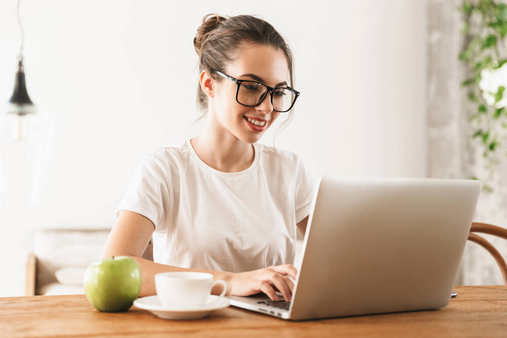 Young woman studying German adjective endings declension on a laptop with coffee and an apple on the table.