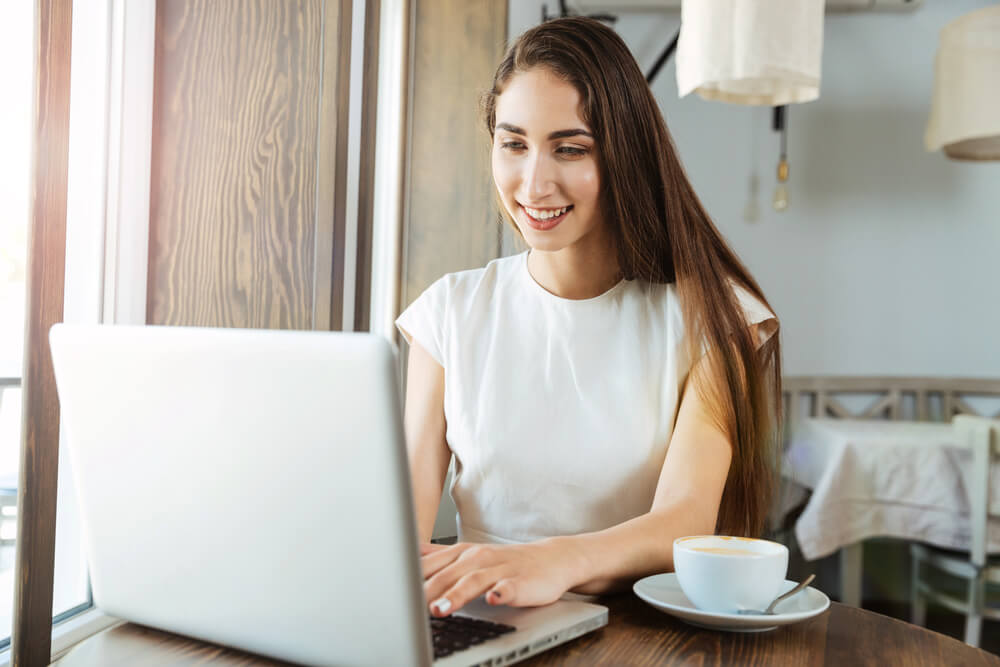 Young woman studying German tenses on a laptop with a cup of coffee.