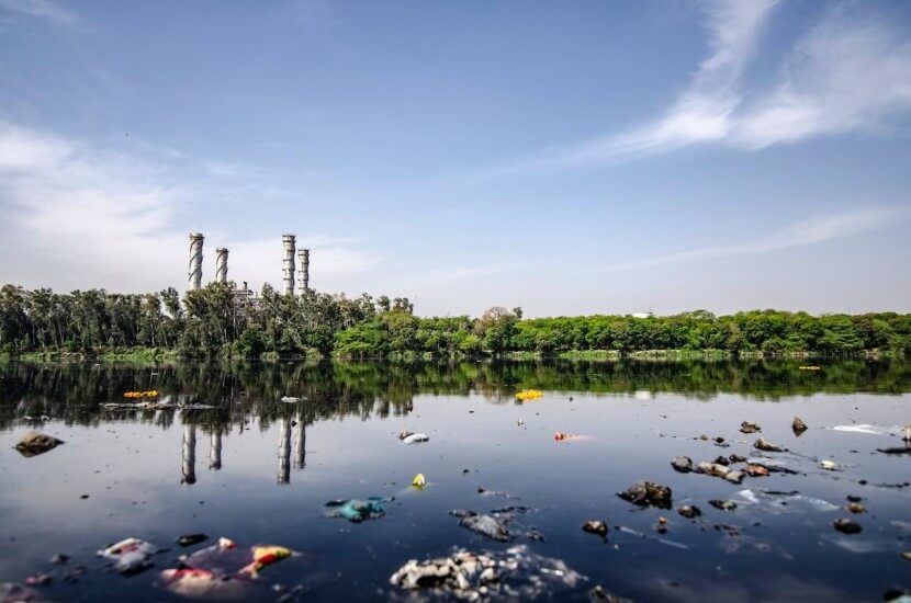 A polluted river with plastic waste and industrial chimneys in the background, representing key terms in German vocabulary for environmental problems.