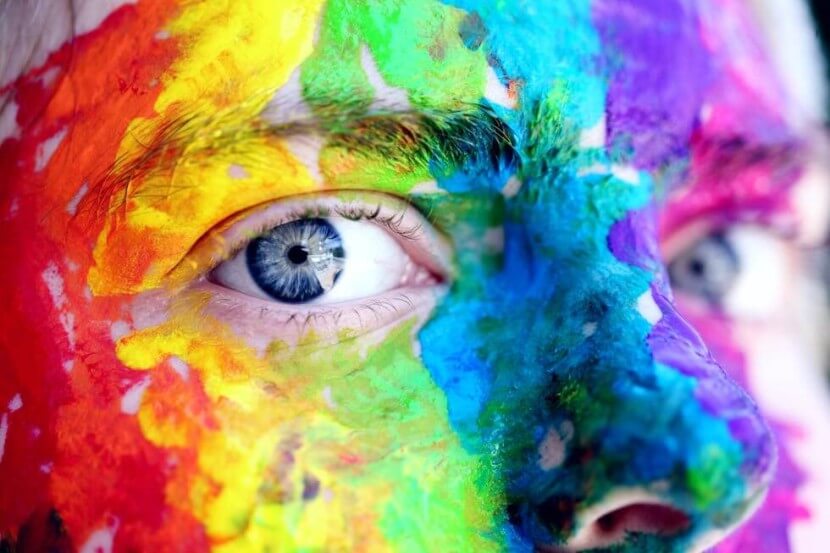 Close-up of a face painted with rainbow colors, representing German colors vocabulary, such as grün (green), lila (purple), and orange (orange).