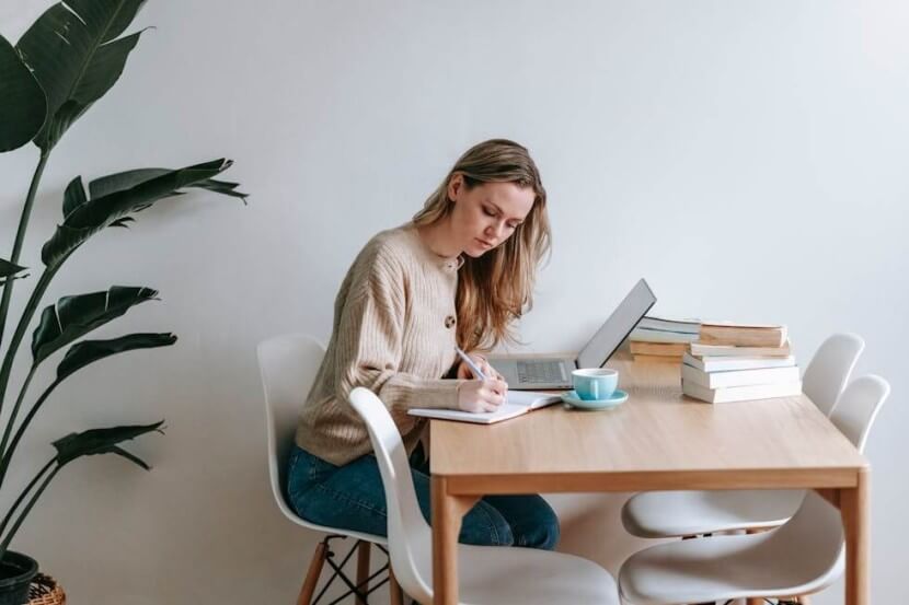 A focused woman studying the German accusative case at a wooden table with a laptop, notebook, and grammar books.