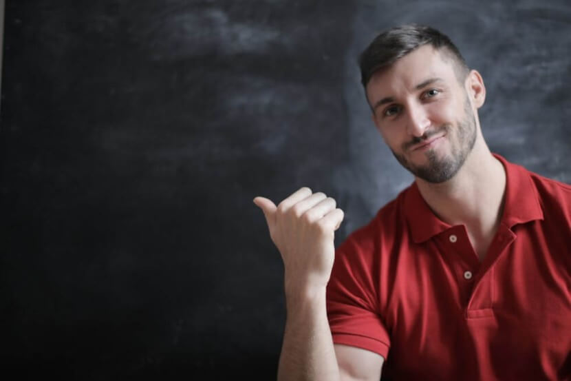 Teacher in a red polo shirt pointing to a chalkboard, representing a German Grammar Articles Overview for learners.