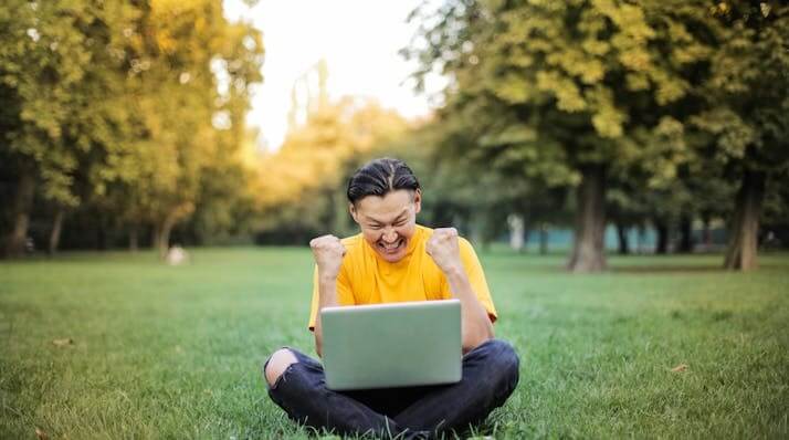 Excited student celebrating success after completing a German Adjectives Vocabulary Quiz on a laptop outdoors.