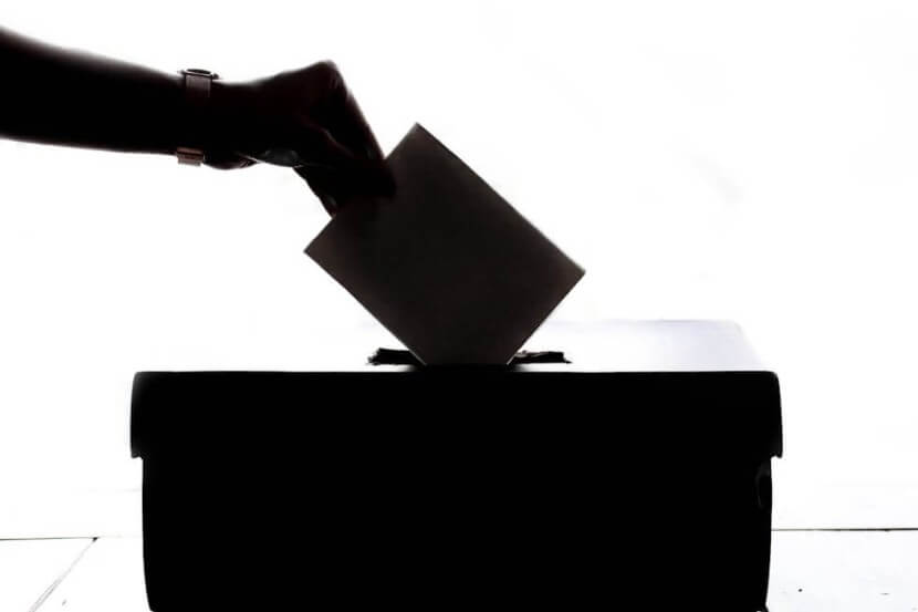 Hand placing a ballot into a voting box, symbolizing democratic processes and related German political vocabulary.