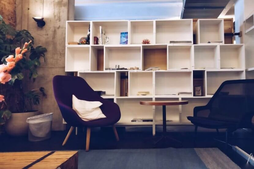 Cozy reading corner with a purple armchair and a white bookshelf, showcasing German furniture vocabulary like Sessel (armchair) and Bücherregal (bookshelf).