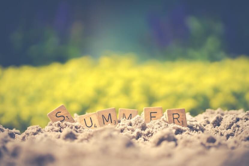 Scrabble tiles spelling 'summer' on sandy ground, illustrating German months vocabulary.