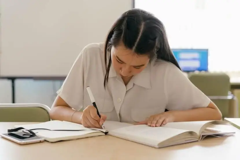 A student writing notes while studying German separable verbs from a textbook to improve grammar skills.