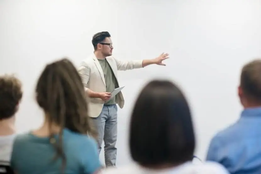 Teacher explaining German inseparable verbs to a class using gestures and a whiteboard.